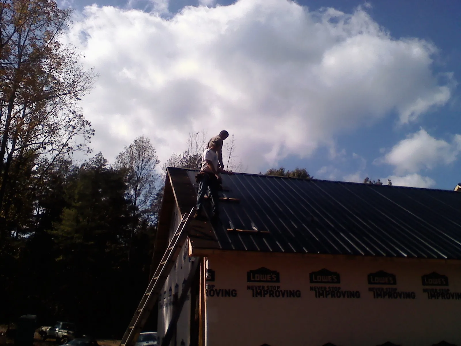 Roofer fastening dark metal panels high against a cloudy sky, from a Roof Inspection job in Spring Run