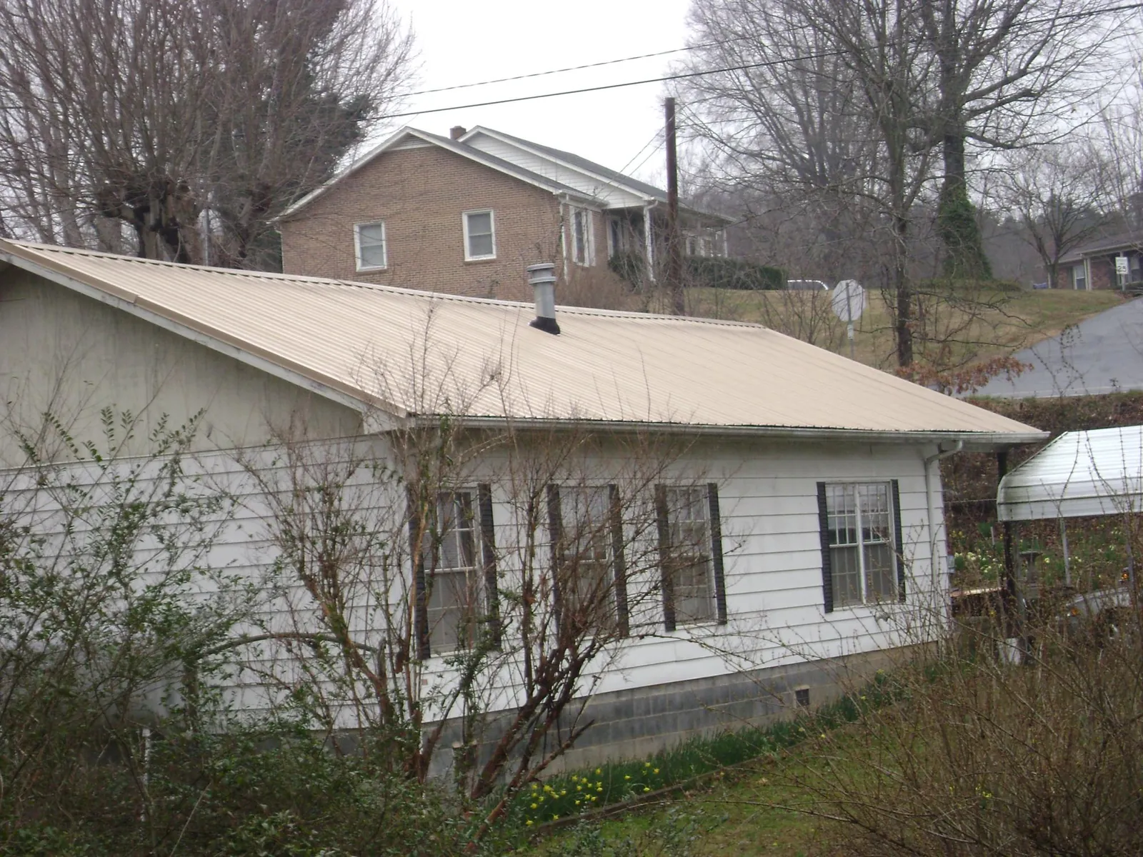 Tan metal roof on a white sided house set into a hillside — Commercial Roofing by Roofing Brothers in Spring Run